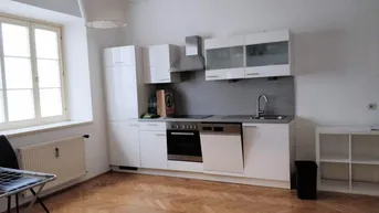 Moderne Einbauküche mit weißen Hochglanzfronten, integrierten Geräten und Fischgrätparkettboden.