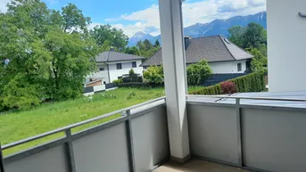 Geräumiger Balkon mit Blick auf grüne Wiesen und die umliegende Berglandschaft unter blauem Himmel.