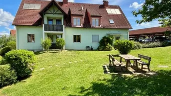 Gepflegtes Einfamilienhaus mit hellgrüner Fassade, Satteldach, Balkon und großem Garten mit Sitzbereich.