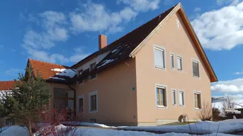 Wohnhaus mit Satteldach und beiger Fassade, umgeben von Schnee unter blauem Himmel.