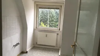 Leere Küche mit Fenster, Heizkörper und Anschlüssen für eine Spüle, mit Blick ins Grüne.