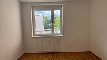 Helles Schlafzimmer mit Parkettboden und großem Fenster, bietet einen angenehmen Ausblick.