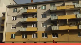 Fassade eines Mehrfamilienhauses mit Balkonen und gelben Akzenten im Sonnenlicht.