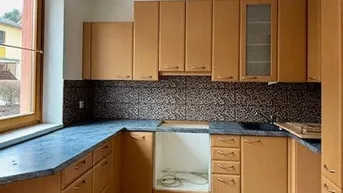 Küche mit Holzschränken, dunkler Arbeitsplatte und gemusterter Rückwand, bereit für Geräte.
