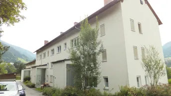 Gebäudeansicht mit heller Fassade, Satteldach und grüner Umgebung in einer ländlichen Gegend.