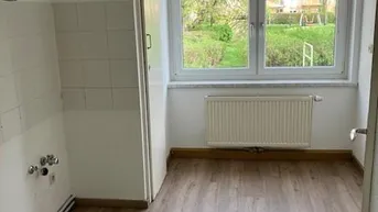 Leere Küche mit Anschlüssen für Geräte, Laminatboden und Blick ins Grüne.