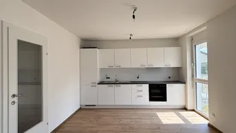 Offener Wohnbereich mit moderner Einbauküche, weißen Schränken und Holzboden, lichtdurchflutet.