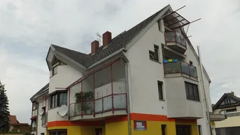 Mehrfamilienhaus mit weißer Fassade, gelben Akzenten und mehreren Balkonen unter bewölktem Himmel.