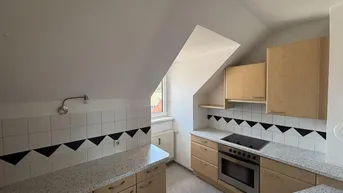 Dachgeschossküche mit heller Holzoptik, Granitarbeitsplatten und integriertem Kochfeld.