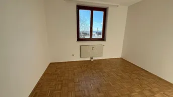 Helles Zimmer mit klassischem Parkettboden, weißen Wänden und einem Fenster mit Weitblick.