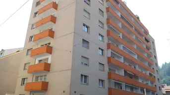 Mehrstöckiges Wohngebäude mit zahlreichen orangefarbenen Balkonen und heller Fassade in städtischer Umgebung.