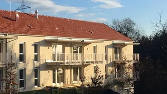 Mehrfamilienhaus mit mehreren Balkonen und angrenzender Grünfläche unter blauem Himmel.