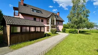 Freistehendes Haus mit rosa Fassade, Ziegeldach und einem großen, gepflegten Garten mit Baumbestand und gepflastertem Weg.