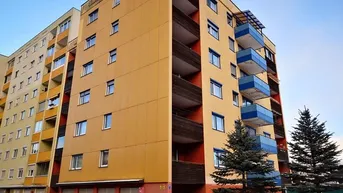 Mehrstöckiges Wohngebäude mit gelber Fassade, blauen Balkonen und Garagen im Erdgeschoss.