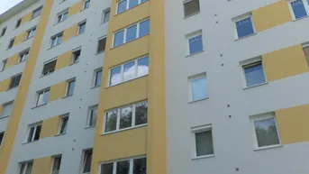 Mehrstöckiges Wohngebäude mit gelben und weißen Fassadenbereichen unter einem bewölkten Himmel.