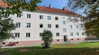 Mehrfamilienhaus mit heller Fassade, roten Dachziegeln und einer gepflegten Grünfläche im Vordergrund.