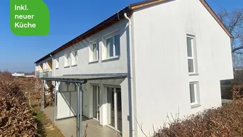 Moderne Reihenhausfassade mit Terrasse und Gartenbereich unter blauem Himmel.