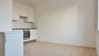 Kompakte Einbauküche mit weißen Schränken, Backofen und freistehendem Kühlschrank in hellem Raum.