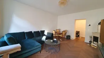 Heller Wohn-Essbereich mit Fischgrätparkett, gemütlicher Sitzecke und traditionellem Kachelofen.