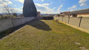 Großer, gepflegter Gartenbereich mit Rasenfläche und umgebender Mauer unter blauem Himmel.