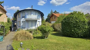 Vorderansicht des Hauses mit gepflegtem Rasen, Sträuchern und einem gepflasterten Weg unter blauem Himmel.