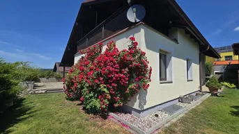 Hausfassade mit blühenden Rosensträuchern und gepflegtem Rasen unter strahlend blauem Himmel.