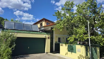 Vorderansicht des Hauses mit Garage, Solaranlage auf dem Dach und üppiger Vegetation.