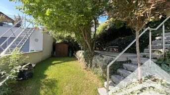 Gepflegter Gartenbereich mit Rasenfläche, Bäumen und einem kleinen Gartenhaus.