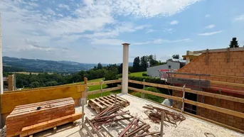 Baustelle mit Rohbau und weitem Blick über die grüne Hügellandschaft unter blauem Himmel.