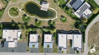 Luftaufnahme des Anwesens mit Teich, modernen Häusern und Photovoltaikanlagen auf den Dächern.