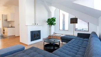 Helles Wohnzimmer mit gemütlichem Sofa, Kamin und Dachschrägenfenster, offen zur Küche.