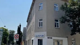 Eckgebäude mit Gewerbefläche im Erdgeschoss und parkenden Autos auf der Straße an einem sonnigen Tag.
