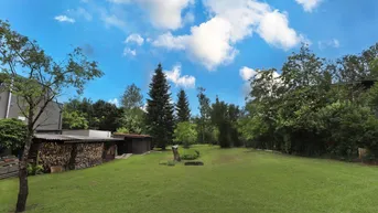 Großer, gepflegter Garten mit weitläufiger Rasenfläche, Baumbestand und Holzschuppen unter blauem Himmel.