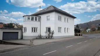 Weißes Wohnhaus mit markantem Rundbau und separater Garage an der Straße.