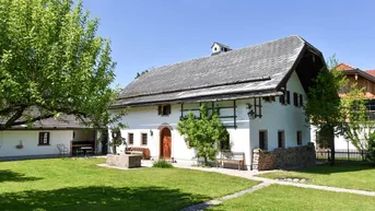 Traditionelles weißes Haus mit grauem Dach, gepflegtem grünen Rasen und altem Baumbestand.