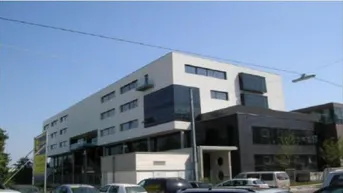 Modernes Bürogebäude mit mehreren Etagen, großen Fenstern und Glasfassadenelementen unter blauem Himmel.