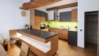 Moderne Küche mit Holzelementen, dunkler Arbeitsplatte und grüner Rückwand, ausgestattet mit Kochinsel.