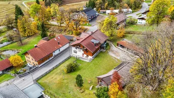 Luftaufnahme eines Anwesens mit mehreren Gebäuden, umgeben von grünen Wiesen und herbstlichen Bäumen.