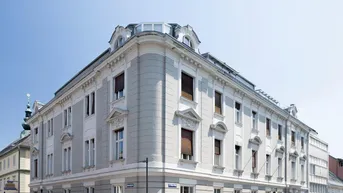 Historisches Eckgebäude mit klassischer Architektur, vielen Fenstern und Mansarddach.