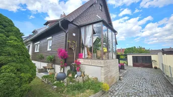 Ansicht des Hauses von der Seite mit einem verglasten Wintergarten und gepflasterter Auffahrt.