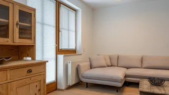 Gemütliches Wohnzimmer mit beigem Ecksofa, rustikalem Couchtisch und hellem Holzschrank.