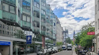Moderne Gebäude mit Glasfassaden entlang einer belebten Straße unter bewölktem Himmel.
