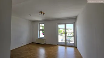 Helles Wohnzimmer mit Parkettboden, großen Fenstern und Zugang zum Balkon.