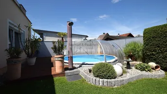 Gepflegter Gartenbereich mit überdachtem Pool, Holzdeck und dekorativen Pflanzen unter blauem Himmel.