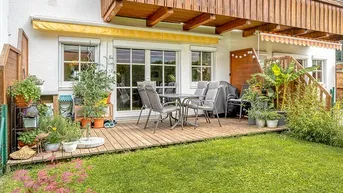 Eine einladende Holzterrasse mit Gartenmöbeln und direktem Zugang zum grünen Rasenbereich.