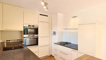 Moderne Einbauküche mit hellen Schränken, dunkler Arbeitsplatte und integrierten Geräten.