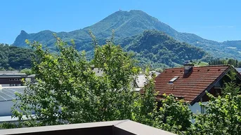 Blick vom Balkon auf die umliegende Berglandschaft und grüne Bäume unter blauem Himmel.
