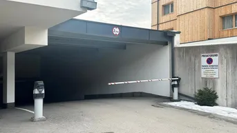 Einfahrt zur Tiefgarage mit Schranke und Höhenbegrenzung, umgeben von moderner Architektur.