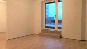 Heller Wohnraum mit Parkettboden und Zugang zu einem Außenbereich über eine große Glastür.