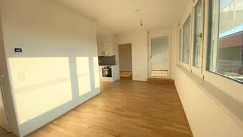 Heller offener Wohnbereich mit Holzboden und integrierter Küchenzeile, ideal für modernes Wohnen.